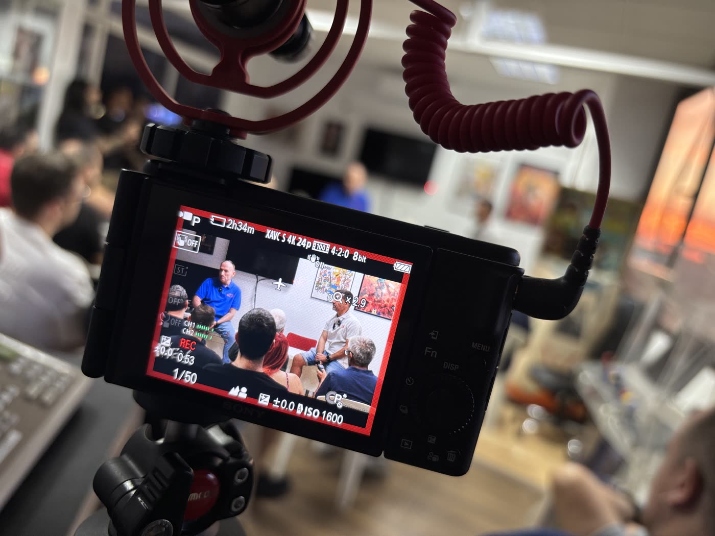 Pantalla de la cámara de PinCasters grabando la charla de presentación, con los ponentes y el público al fondo