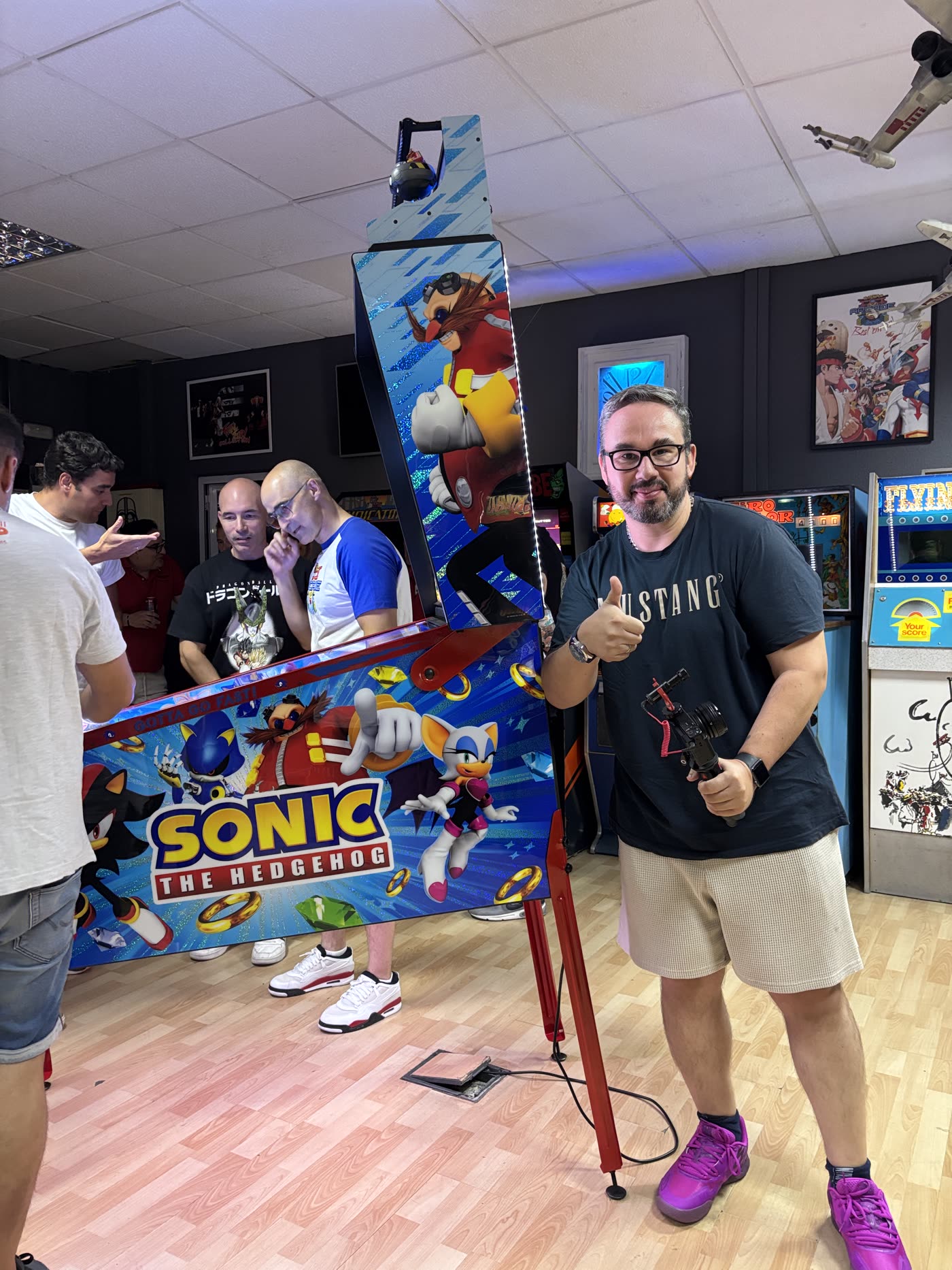 Rober junto al Sonic the Hedgehog de Jersey Jack Pinball haciendo el gesto del pulgar hacia arriba, mientras otros asistentes juegan y miran la máquina