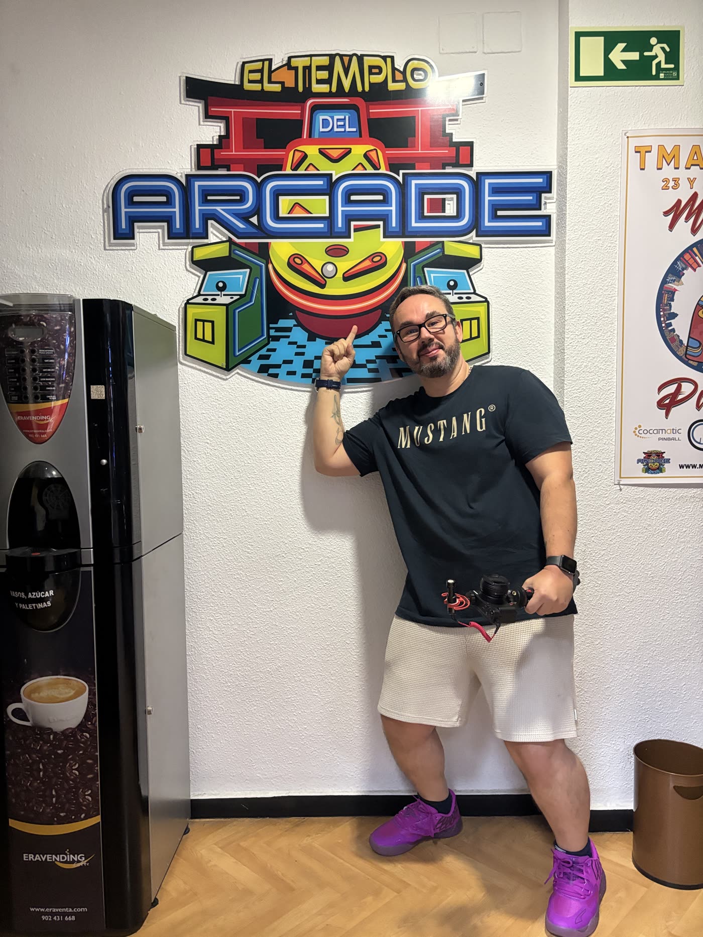 Rober, de PinCasters, señalando el logo de El Templo del Arcade en la pared del local, con la cámara de grabación en la mano