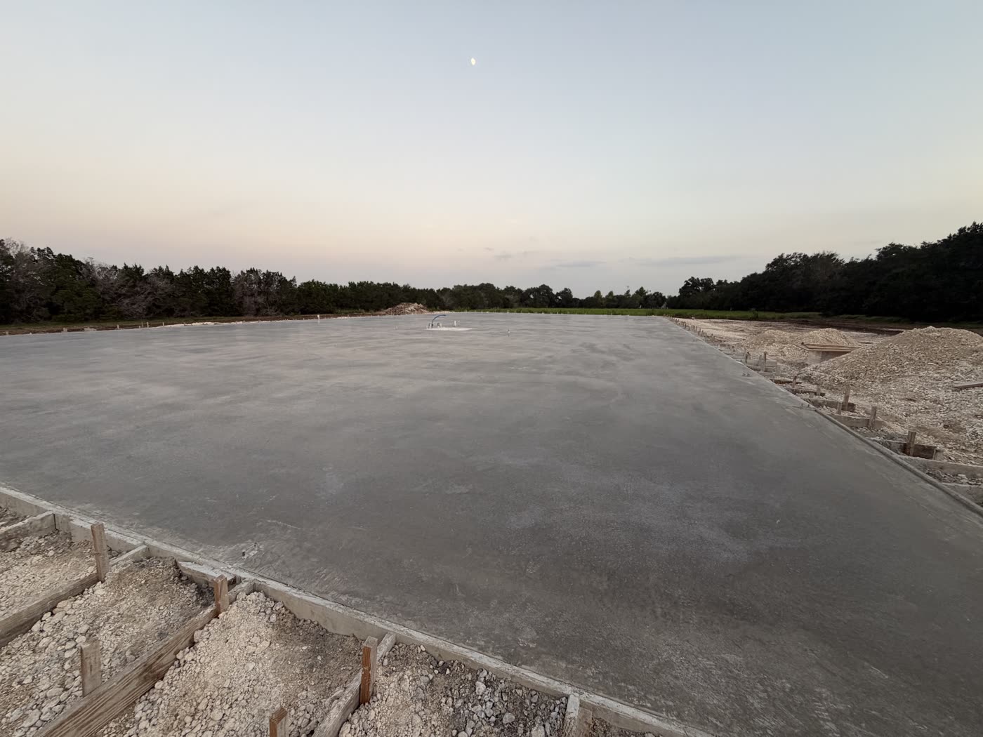 Losa de hormigón ya terminada y curando, al atardecer, en el solar de la futura fábrica